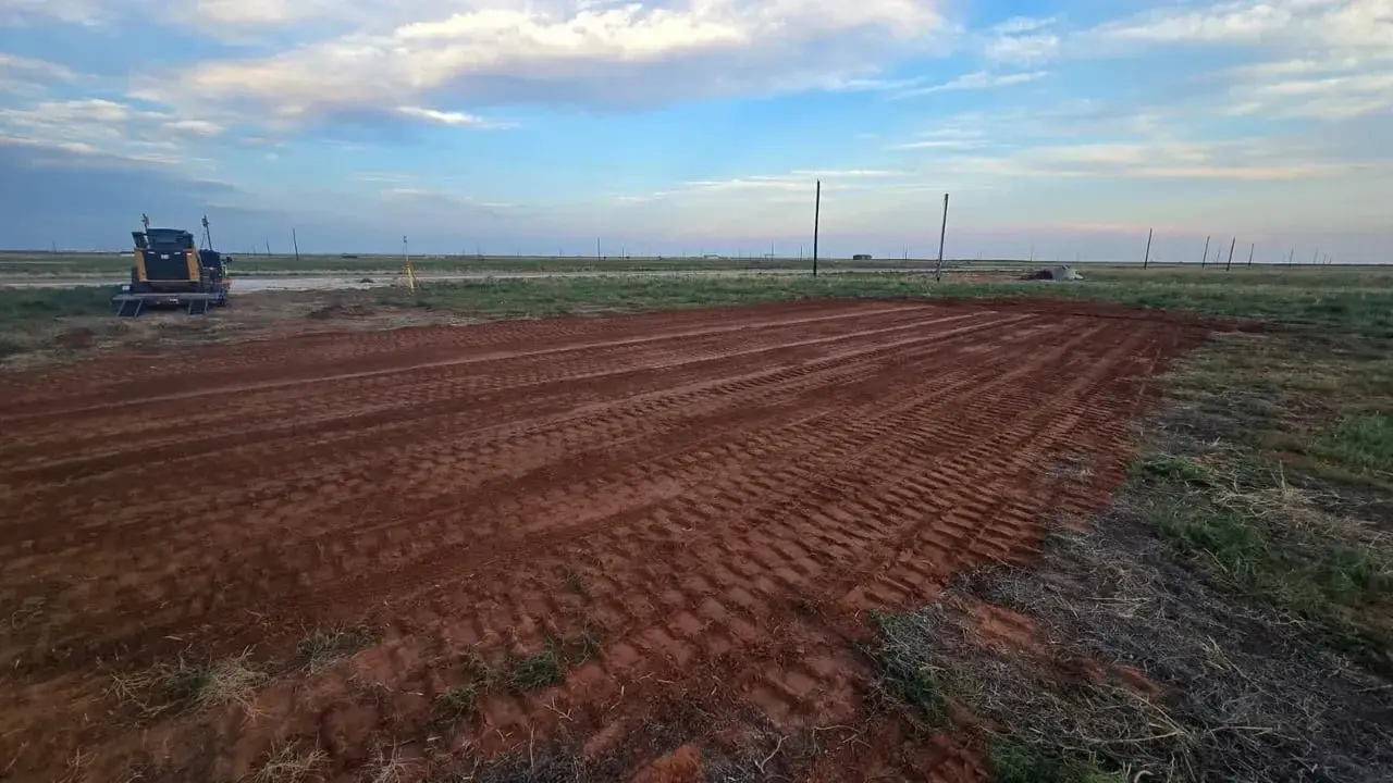 A cleared and rough-graded red dirt pad in an open field at dusk