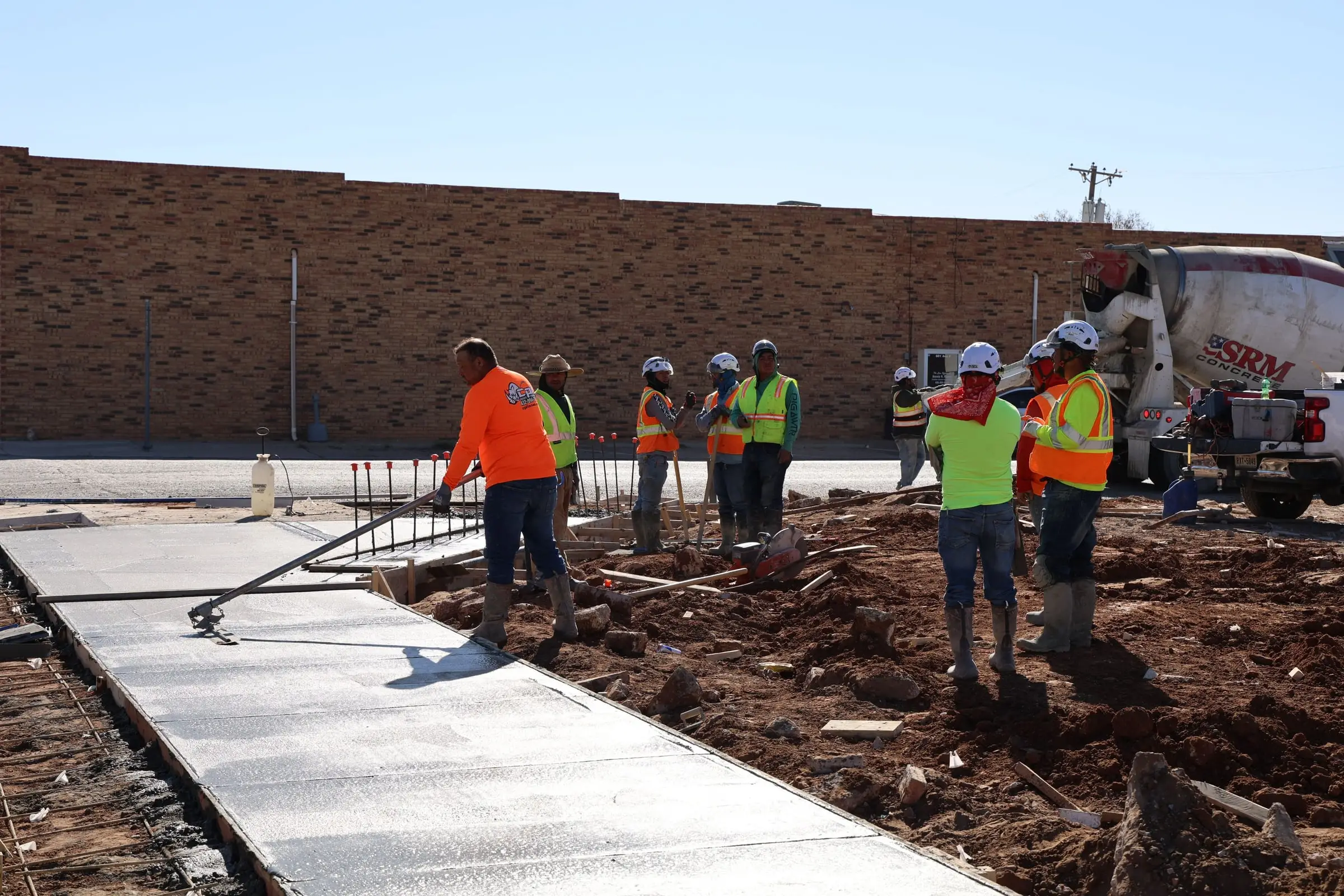 Crew finishing a freshly poured concrete slab beside a ready-mix truck