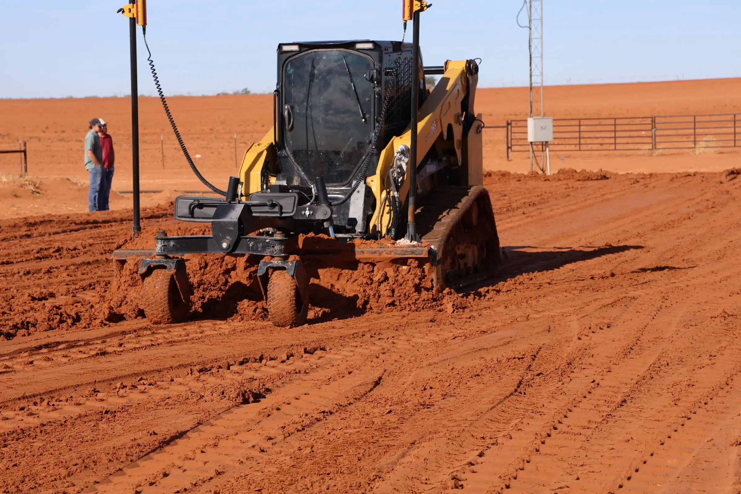 Compact track loader with a laser-guided grade box leveling red dirt