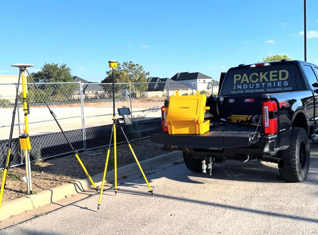 Packed Industries pickup parked beside survey equipment set up on yellow tripods