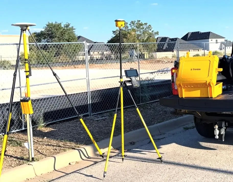 Survey equipment on yellow tripods beside a yellow equipment case on a pickup tailgate