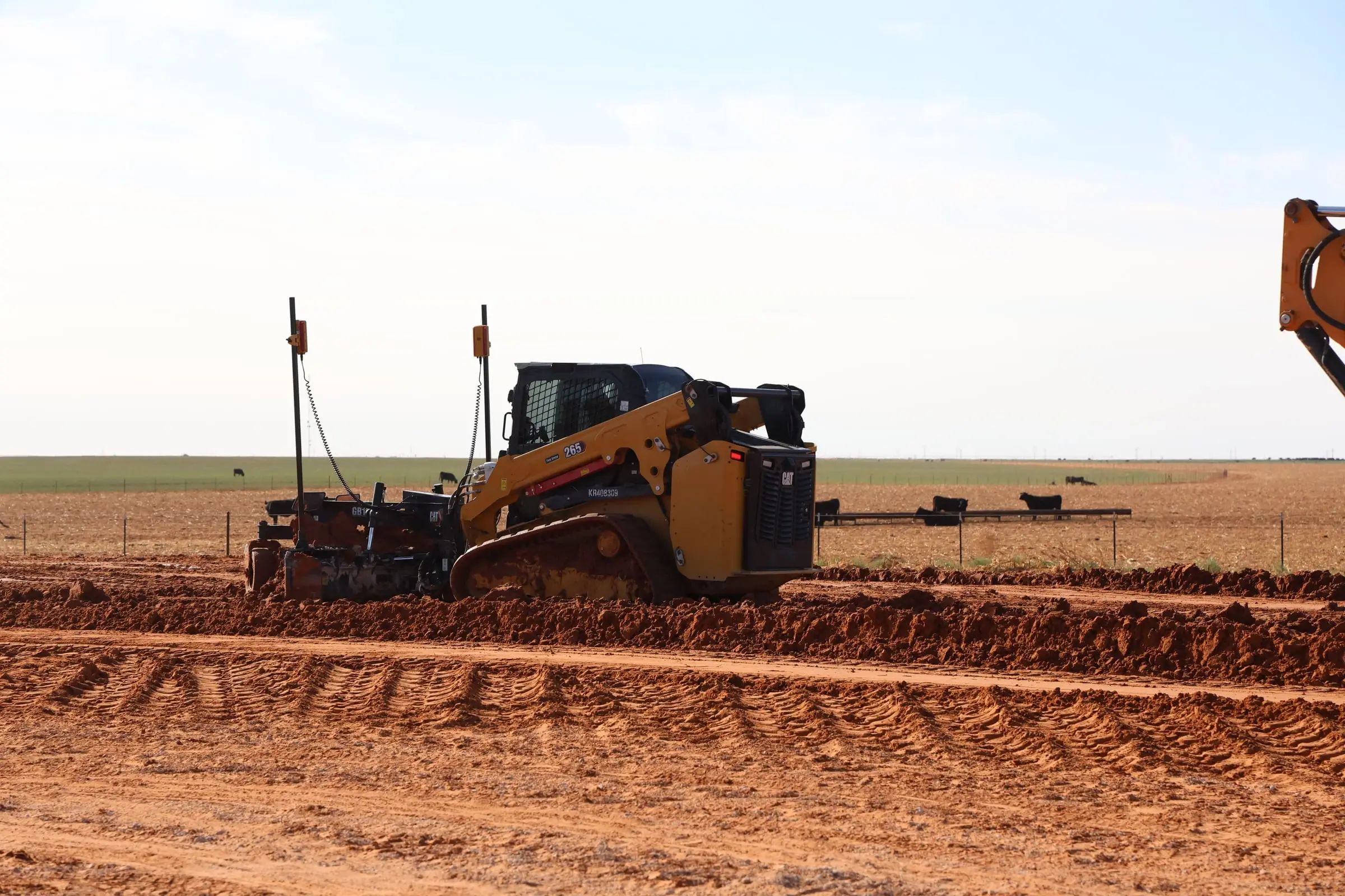 Compact track loader with a grade box shaping a dirt pad at the edge of a pasture