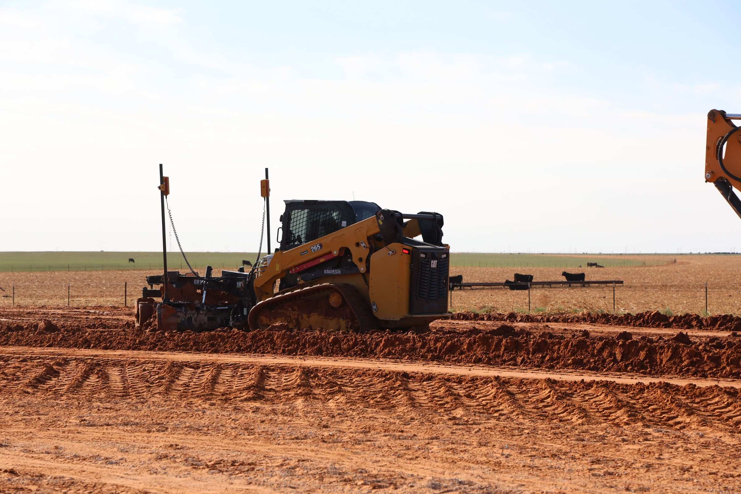 Compact track loader with a grade box shaping a dirt pad at the edge of a pasture