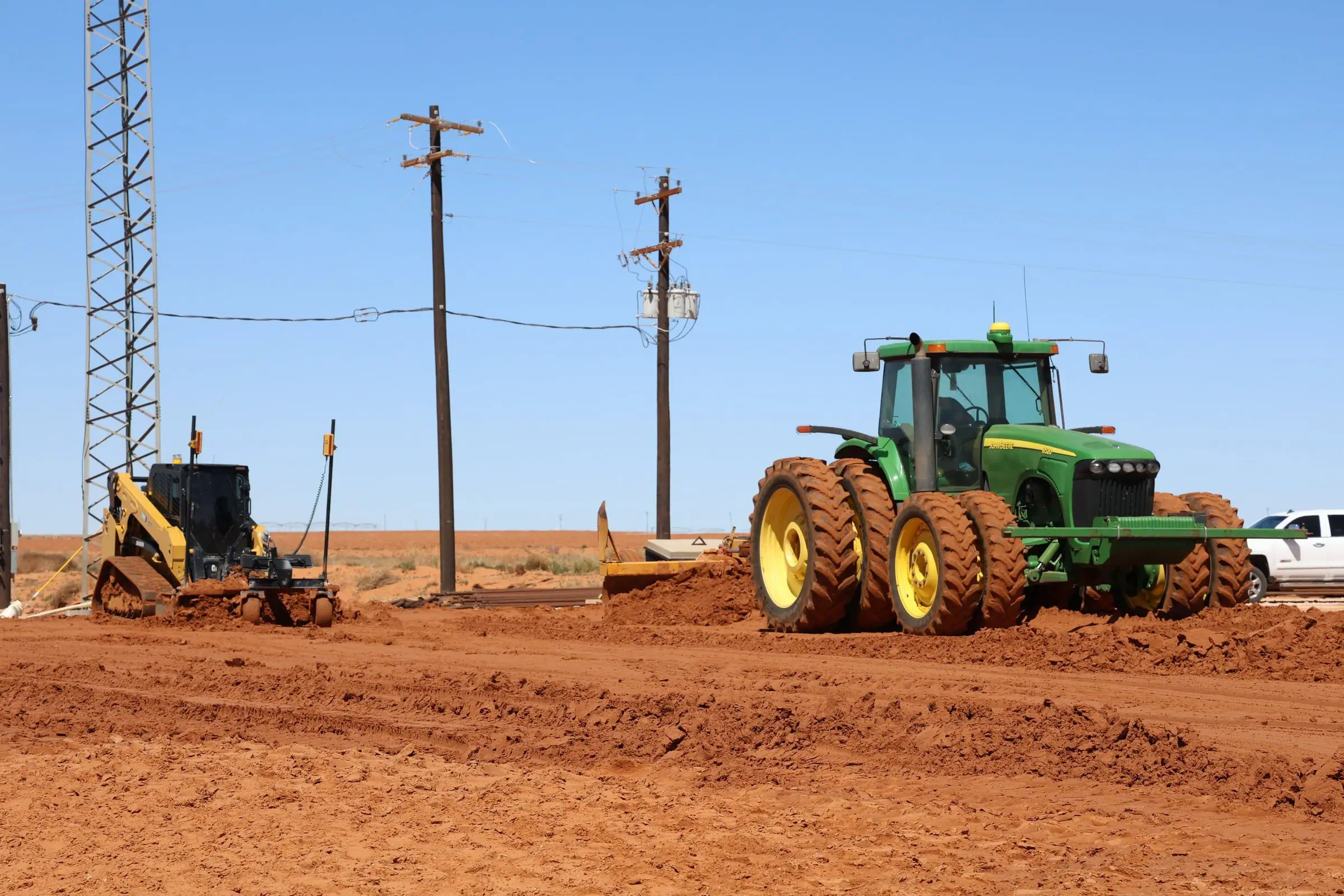 Farm tractor pulling a scraper alongside a compact track loader on graded red dirt
